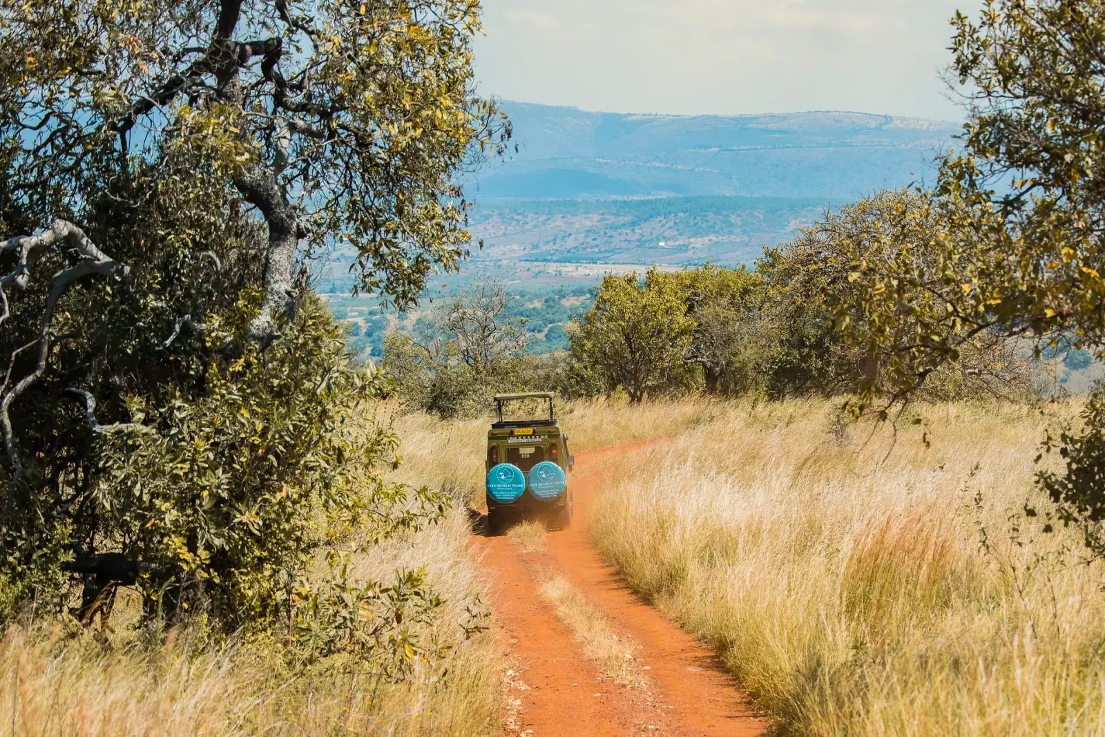 Safari vehicle on a dirt track through Akagera, with a lake in the distance